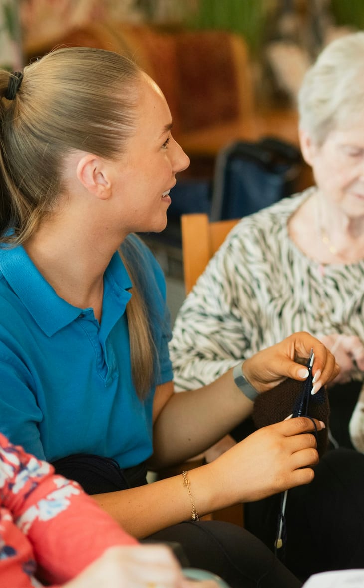 A caregiver holding hands with a senior woman in her living room